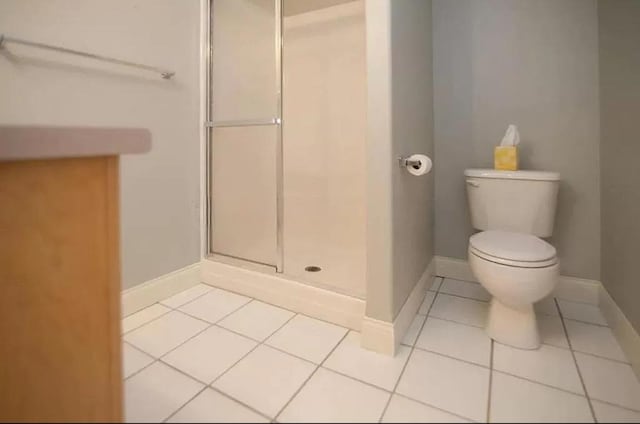 bathroom featuring a shower stall, toilet, tile patterned flooring, and baseboards