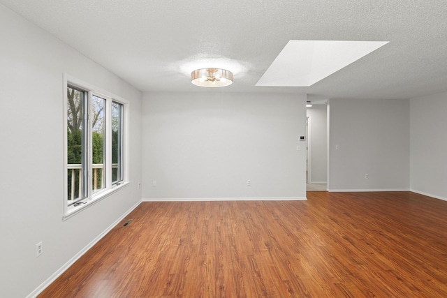 unfurnished room with a textured ceiling, visible vents, a skylight, wood finished floors, and baseboards