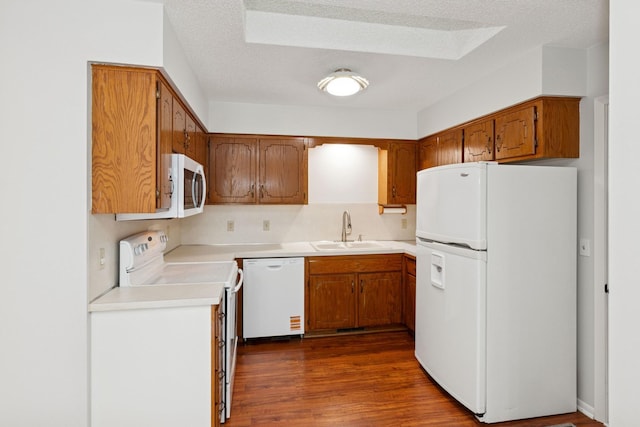 kitchen featuring brown cabinets, a sink, light countertops, white appliances, and dark wood-type flooring