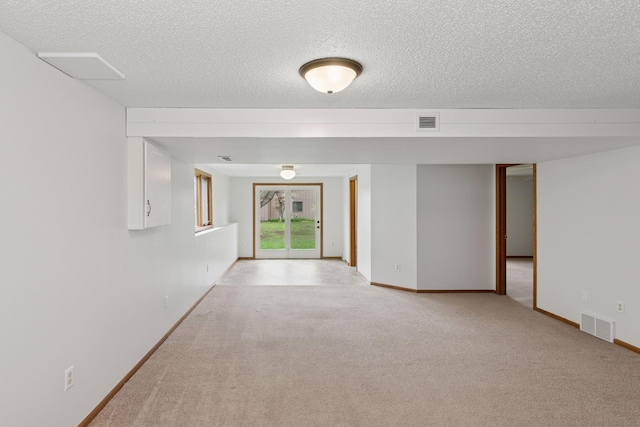 empty room featuring a textured ceiling, visible vents, and light carpet