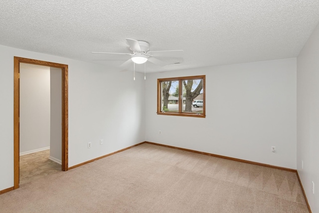 spare room with a ceiling fan, a textured ceiling, light colored carpet, and baseboards