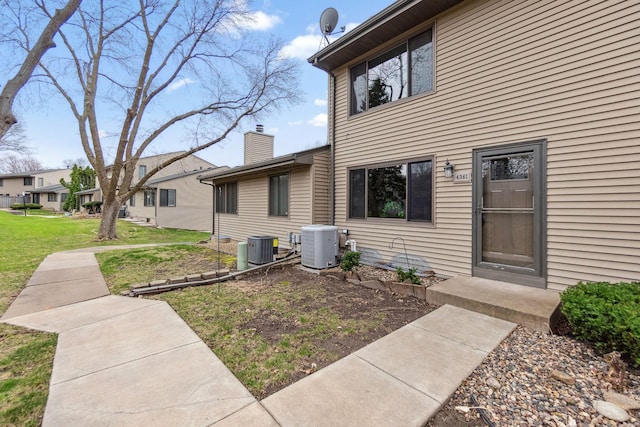 view of exterior entry featuring a yard, cooling unit, and a chimney