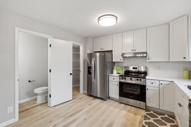 kitchen with light wood-type flooring, under cabinet range hood, white cabinets, appliances with stainless steel finishes, and backsplash