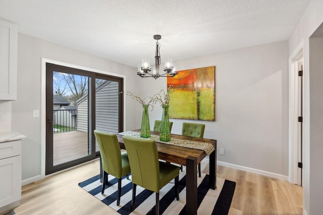 dining area featuring light wood-style floors, baseboards, a textured ceiling, and a chandelier