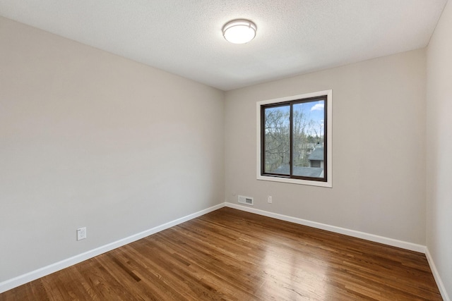 unfurnished room with baseboards, visible vents, and wood finished floors