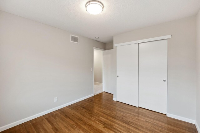 unfurnished bedroom featuring a textured ceiling, visible vents, wood finished floors, baseboards, and a closet