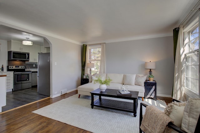 living area featuring arched walkways, visible vents, dark wood-style flooring, and baseboards