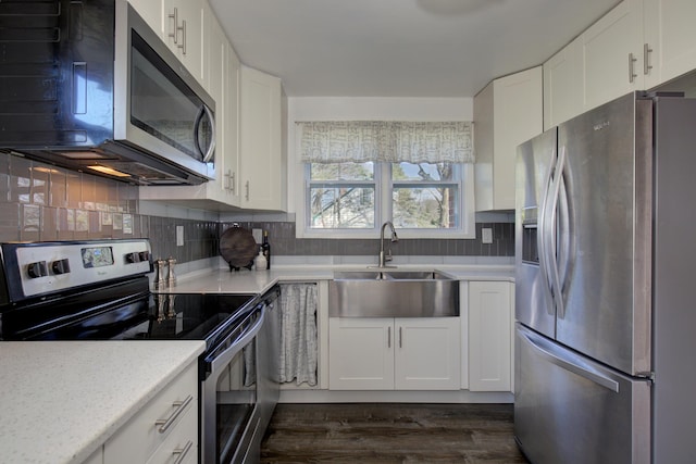 kitchen with appliances with stainless steel finishes, white cabinets, backsplash, a sink, and dark wood-style floors