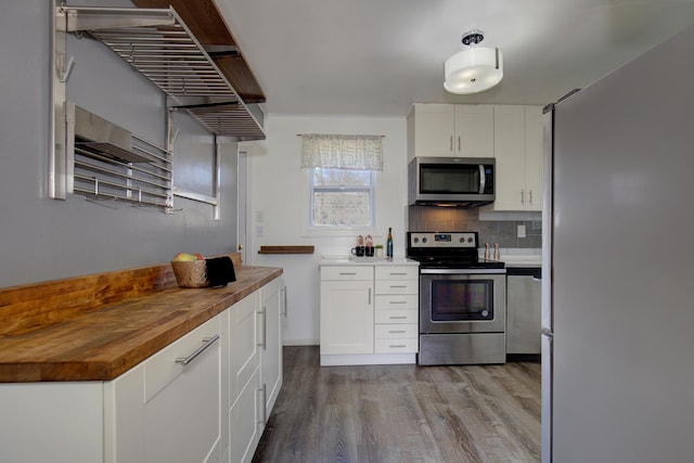 kitchen featuring tasteful backsplash, wood finished floors, wood counters, stainless steel appliances, and white cabinets