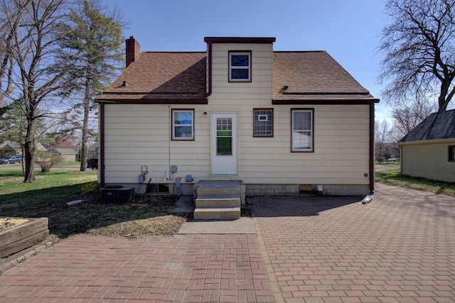 rear view of property featuring a shingled roof and a chimney