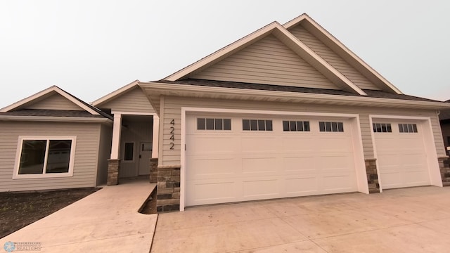 4242 Bristlecone Loop S, Fargo, ND 58104 - view of front facade with driveway, stone siding, a garage, an outbuilding, and a shingled roof