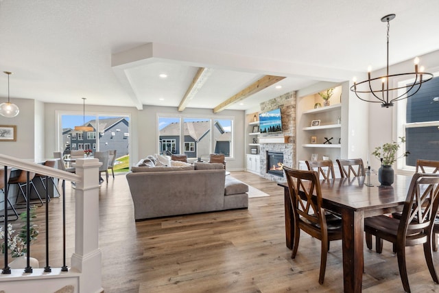 dining area featuring wood finished floors, a fireplace, a notable chandelier, built in features, and beamed ceiling
