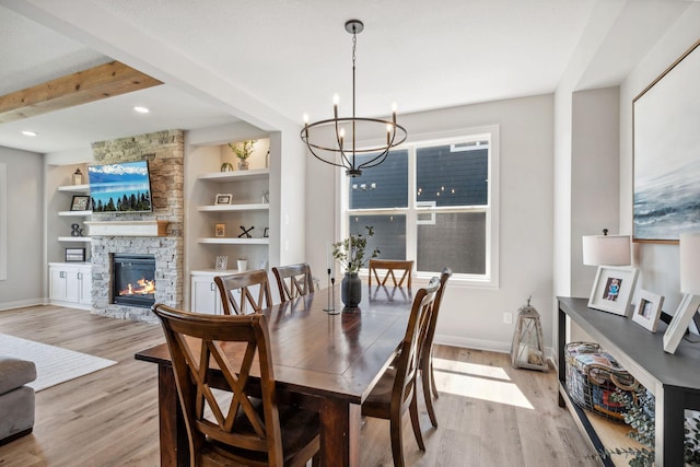 dining area featuring baseboards, a fireplace, an inviting chandelier, and light wood-type flooring