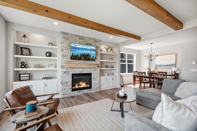 living area with beam ceiling, a fireplace, a notable chandelier, light wood-style floors, and built in shelves