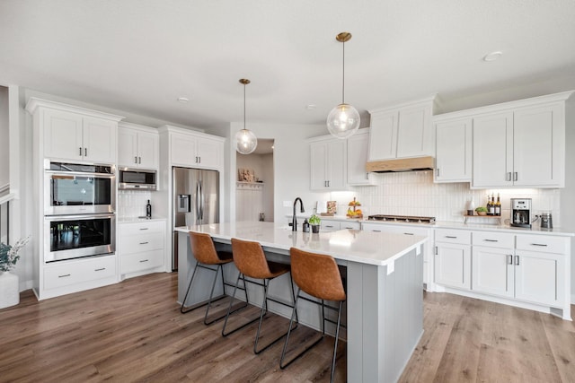 kitchen featuring stainless steel appliances, white cabinets, light wood-type flooring, and decorative backsplash