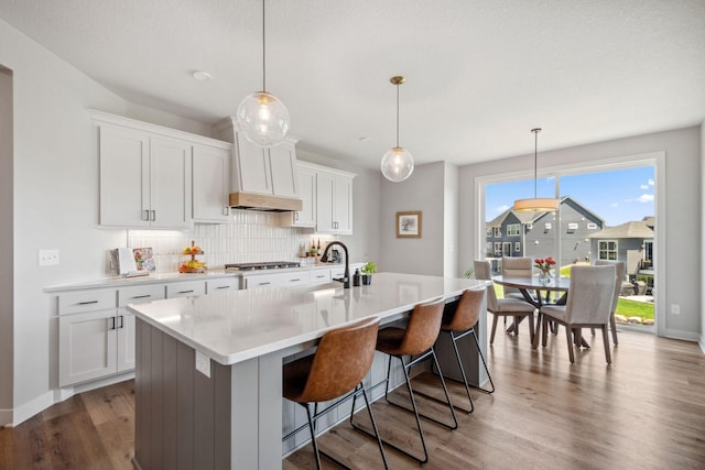 kitchen featuring stainless steel gas cooktop, custom range hood, a kitchen bar, decorative backsplash, and a center island with sink