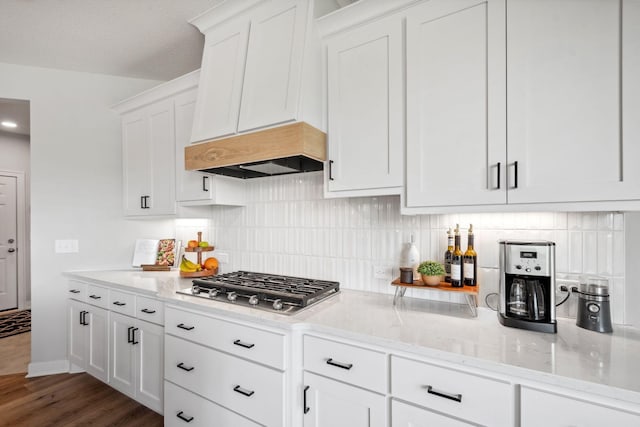 kitchen with light stone countertops, stainless steel gas stovetop, white cabinetry, wood finished floors, and backsplash