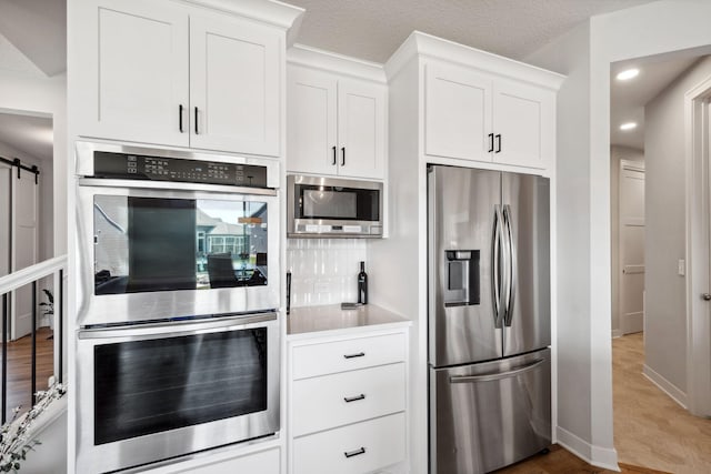 kitchen with light wood-style floors, stainless steel appliances, white cabinets, and a barn door