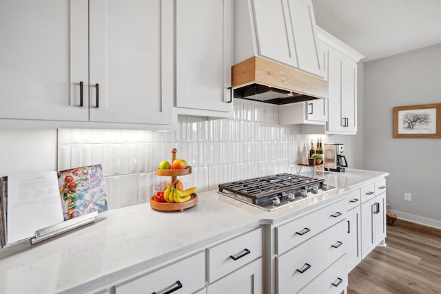 kitchen with white cabinetry, light stone countertops, light wood-style floors, decorative backsplash, and stainless steel gas cooktop