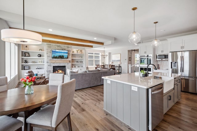 kitchen with light wood-style flooring, a sink, a center island with sink, stainless steel appliances, and a fireplace