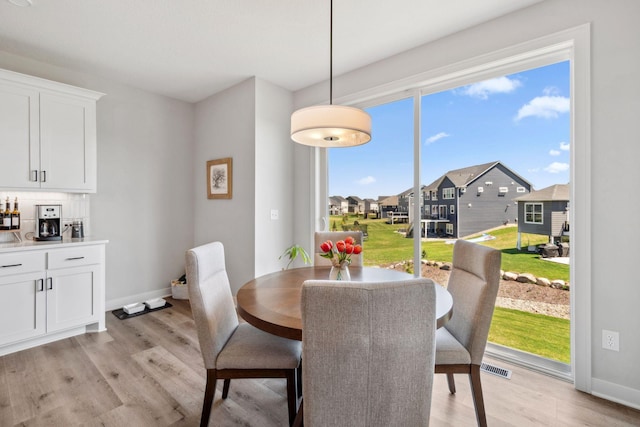 dining space featuring light wood finished floors, a residential view, visible vents, baseboards, and bar area