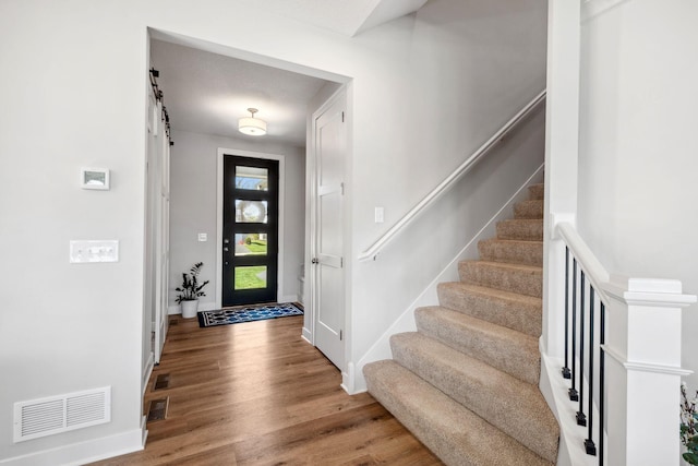 foyer featuring baseboards, stairs, visible vents, and wood finished floors
