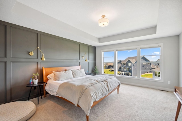 bedroom with light colored carpet and a raised ceiling