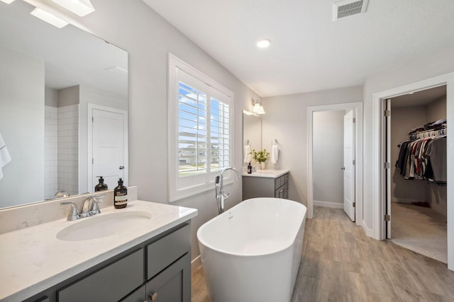 full bathroom with visible vents, a sink, a freestanding tub, wood finished floors, and a spacious closet