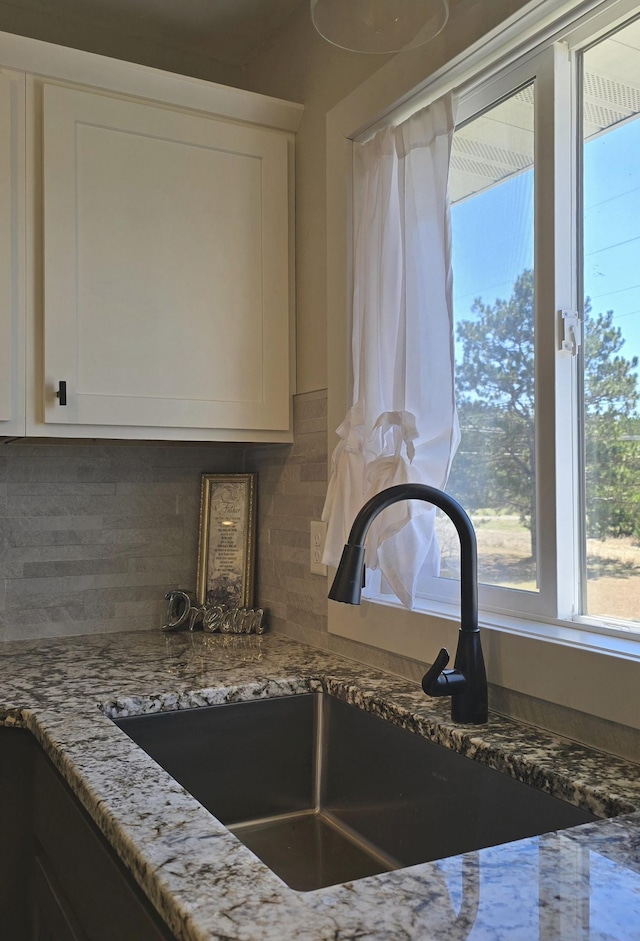 1138 Pleasant Ct SW, Bemidji Twp, MN 56601 - details featuring backsplash, white cabinetry, light stone countertops, and a sink