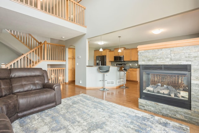 living room featuring a high ceiling, a fireplace, arched walkways, baseboards, and wood finished floors