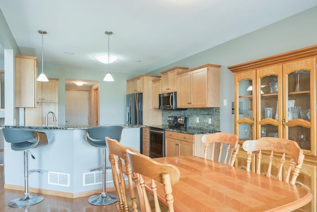 kitchen featuring light brown cabinetry, decorative backsplash, stainless steel appliances, and light wood-style flooring