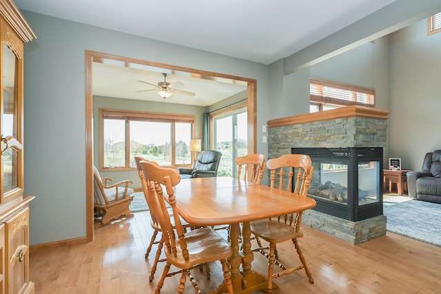 dining area featuring a ceiling fan, baseboards, light wood finished floors, and a fireplace