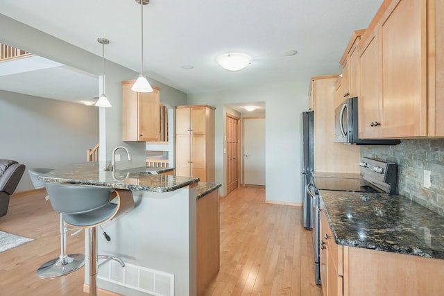 kitchen featuring light brown cabinetry, appliances with stainless steel finishes, a sink, a breakfast bar area, and a peninsula