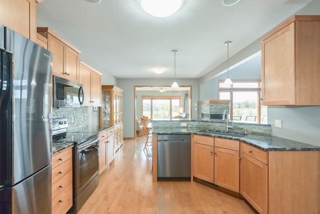 kitchen featuring a sink, light wood-style floors, dark stone counters, stainless steel appliances, and decorative backsplash