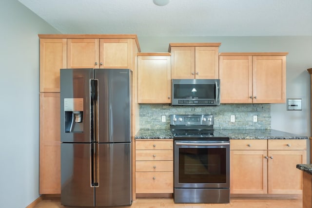 kitchen featuring stainless steel appliances, dark stone countertops, tasteful backsplash, and light brown cabinets
