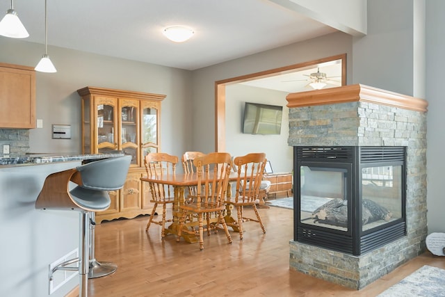 dining area with a ceiling fan, light wood-type flooring, and a stone fireplace