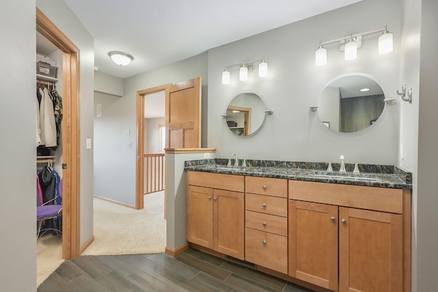 full bathroom with wood finish floors, a sink, a walk in closet, double vanity, and baseboards