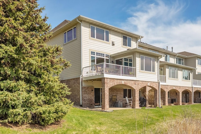 rear view of house with brick siding, a patio area, a balcony, central air condition unit, and a yard