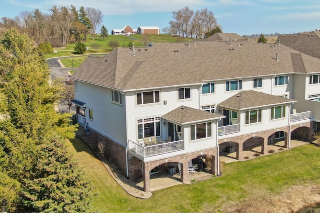 rear view of property featuring a sunroom, a shingled roof, a patio area, and a yard