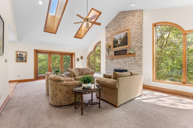 carpeted living area with a skylight, ceiling fan, a brick fireplace, high vaulted ceiling, and baseboards