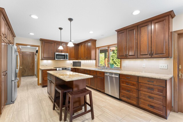 kitchen featuring stainless steel appliances, a sink, decorative backsplash, a center island, and light stone counters