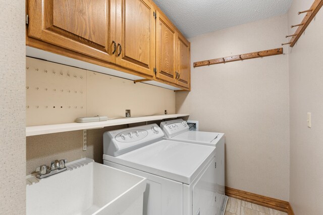 laundry room with washing machine and clothes dryer, cabinet space, baseboards, and a textured ceiling