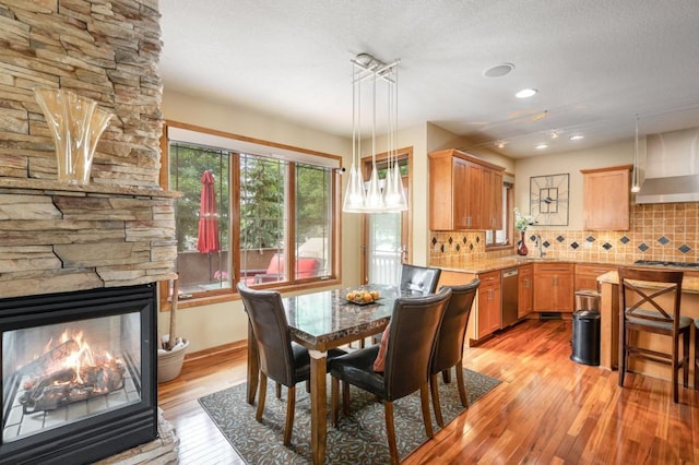 dining room with recessed lighting, light wood-type flooring, a textured ceiling, and a stone fireplace
