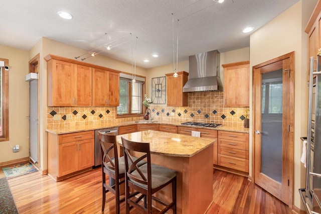 kitchen featuring a center island, a sink, stainless steel appliances, light wood-style flooring, and wall chimney exhaust hood