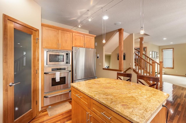 kitchen featuring a warming drawer, light wood finished floors, appliances with stainless steel finishes, light stone countertops, and a kitchen island