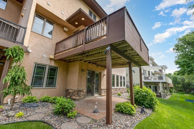 rear view of property featuring stucco siding, stone siding, a patio, and a lawn