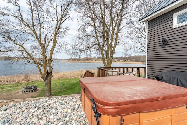wooden deck with a lawn, a water view, a hot tub, and an outdoor fire pit