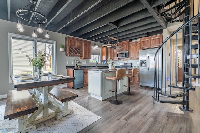 kitchen featuring dark countertops, appliances with stainless steel finishes, a sink, light wood finished floors, and a kitchen island