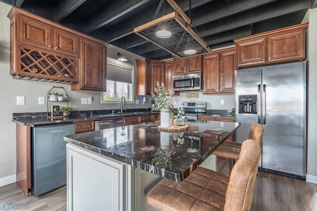 kitchen with a breakfast bar, light wood-type flooring, dark stone counters, a sink, and stainless steel appliances