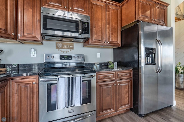 kitchen featuring stainless steel appliances, dark countertops, brown cabinetry, and dark wood-type flooring